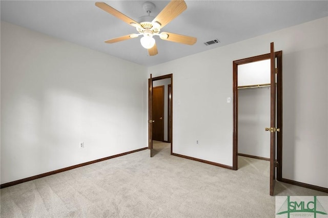 unfurnished bedroom featuring light carpet, a walk in closet, a closet, and ceiling fan