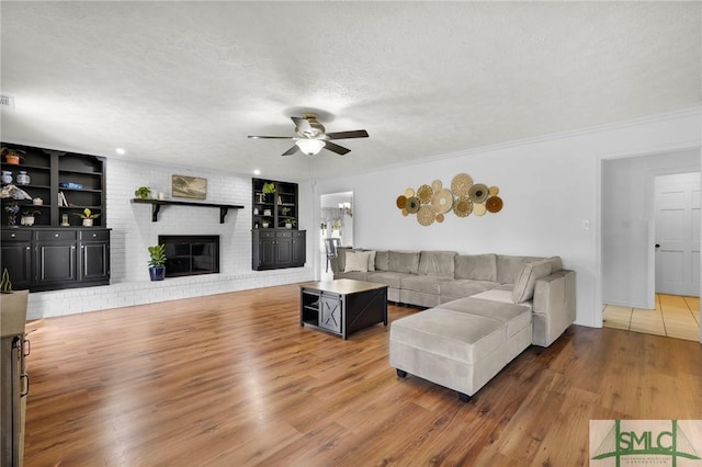 living room with built in features, a fireplace, hardwood / wood-style flooring, ceiling fan, and a textured ceiling