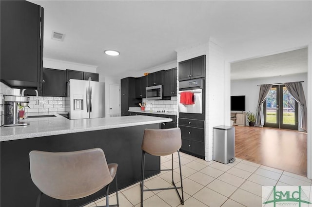 kitchen featuring appliances with stainless steel finishes, a kitchen breakfast bar, light tile patterned floors, kitchen peninsula, and french doors