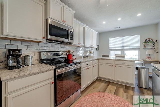 kitchen featuring visible vents, light wood-style flooring, decorative backsplash, appliances with stainless steel finishes, and a textured ceiling