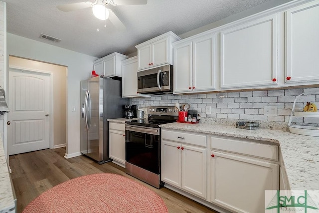 kitchen with ceiling fan, stainless steel appliances, white cabinetry, light wood-style floors, and backsplash