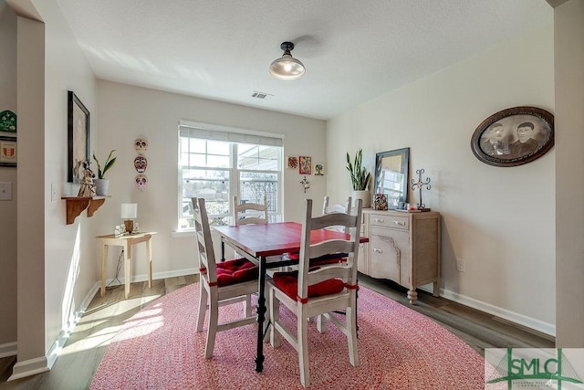 dining area featuring a textured ceiling, wood finished floors, visible vents, and baseboards