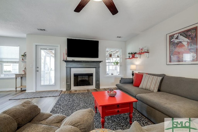 living room with a fireplace with flush hearth, a textured ceiling, wood finished floors, and visible vents