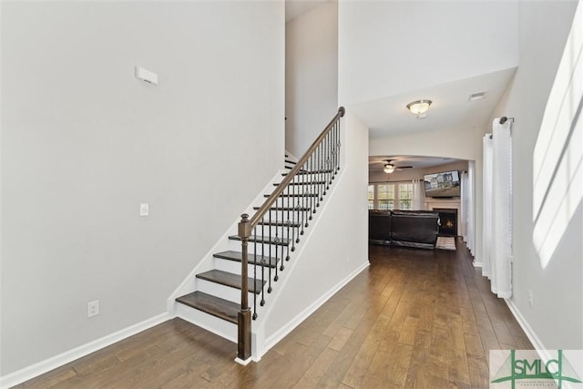 staircase featuring wood-type flooring, ceiling fan, and a high ceiling