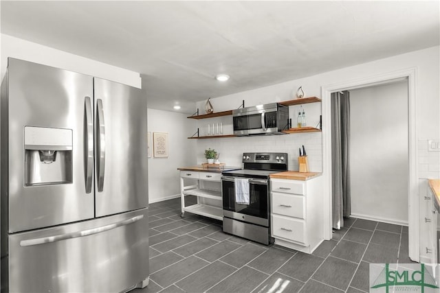 kitchen featuring appliances with stainless steel finishes, wood counters, tasteful backsplash, white cabinetry, and dark tile patterned floors