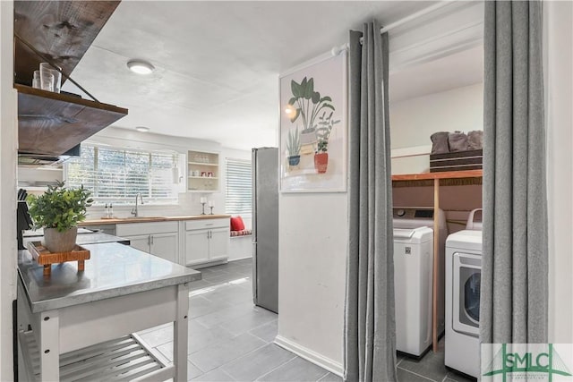 kitchen featuring washing machine and clothes dryer, sink, white cabinetry, light tile patterned floors, and stainless steel fridge