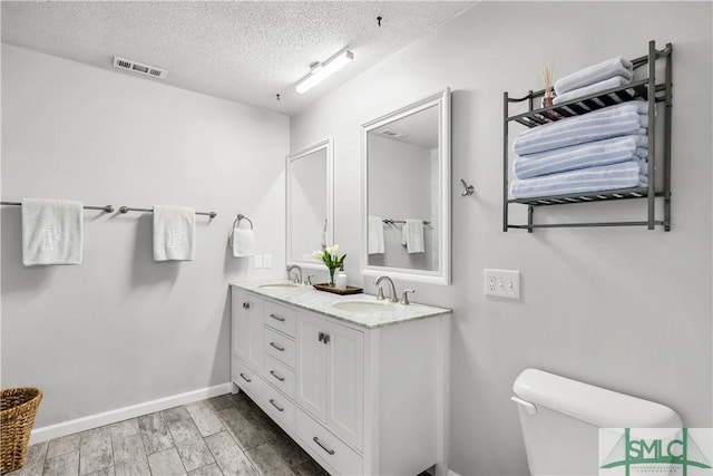 bathroom featuring wood-type flooring, vanity, a textured ceiling, and toilet