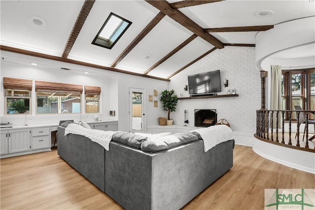 living room featuring a fireplace, brick wall, vaulted ceiling with skylight, and light hardwood / wood-style flooring