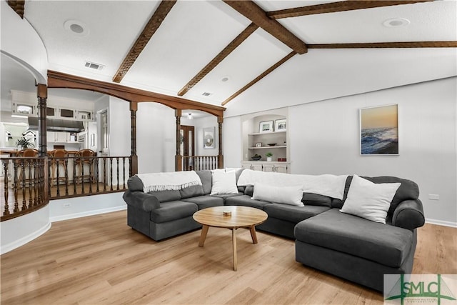 living room with vaulted ceiling with beams, built in features, and light wood-type flooring