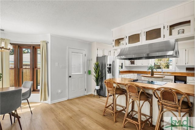 kitchen with butcher block counters, decorative light fixtures, light wood-type flooring, stainless steel fridge, and white cabinets