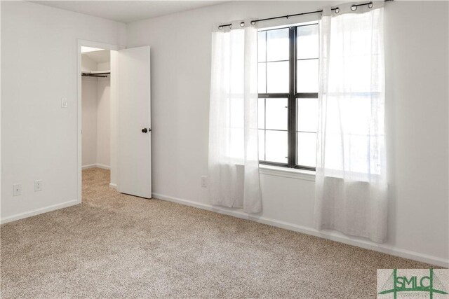 unfurnished bedroom featuring a walk in closet, light colored carpet, and a closet