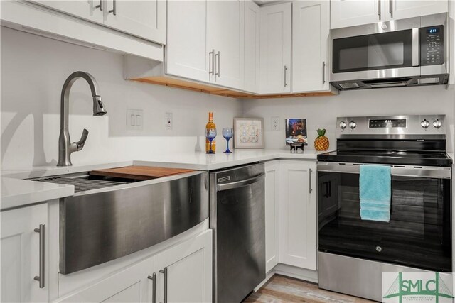 kitchen with appliances with stainless steel finishes, light hardwood / wood-style floors, and white cabinets