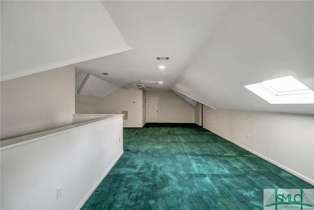 additional living space with dark colored carpet, vaulted ceiling with skylight, and ceiling fan