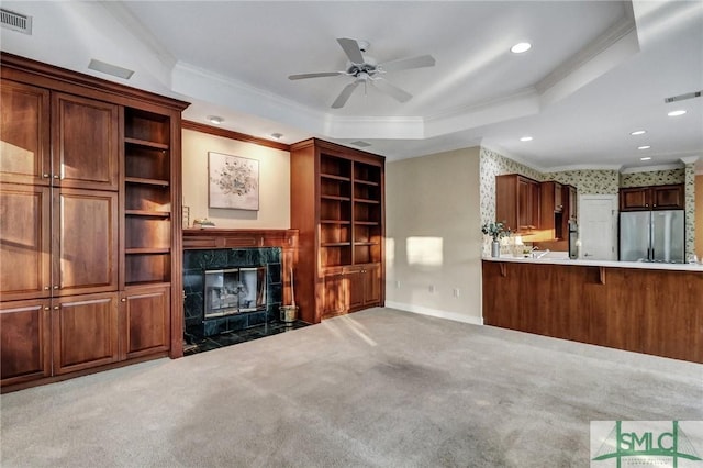 unfurnished living room with crown molding, ceiling fan, a tray ceiling, a fireplace, and carpet floors