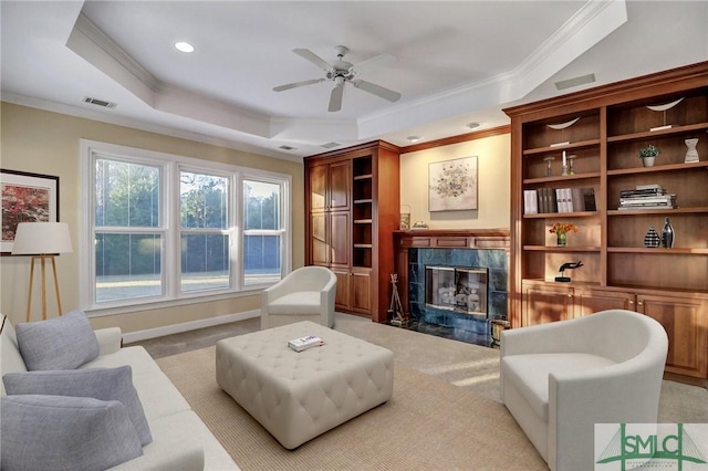 carpeted living room with ceiling fan, ornamental molding, a high end fireplace, and a tray ceiling