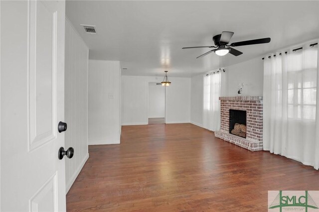 unfurnished living room featuring a brick fireplace, dark hardwood / wood-style floors, and ceiling fan