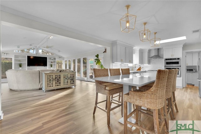 dining space with ceiling fan, sink, light hardwood / wood-style floors, and vaulted ceiling with beams