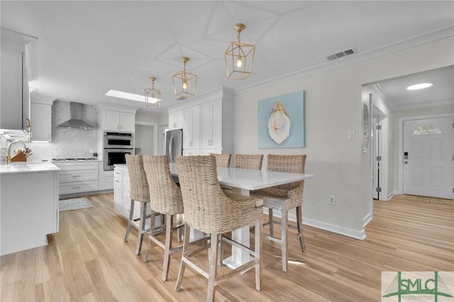 dining room featuring a skylight, ornamental molding, and light wood-type flooring