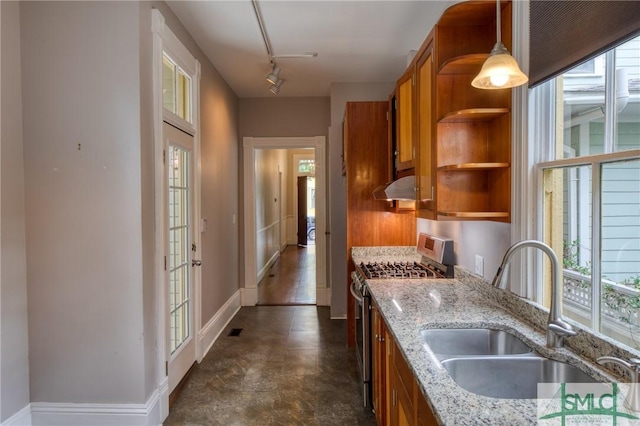 kitchen featuring sink, stainless steel gas range, rail lighting, light stone countertops, and decorative light fixtures