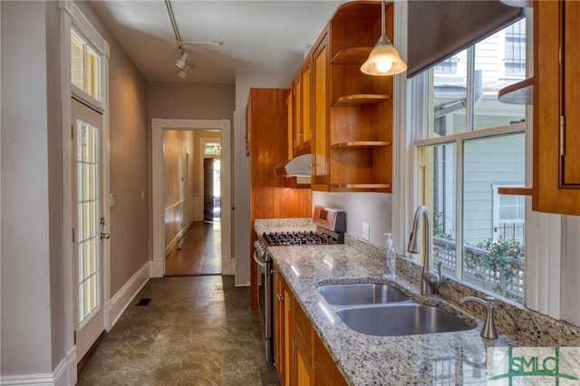 kitchen featuring sink, rail lighting, stainless steel gas stove, light stone counters, and decorative light fixtures