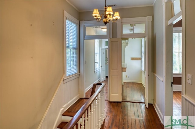 doorway to outside with crown molding, dark wood-type flooring, a wealth of natural light, and an inviting chandelier