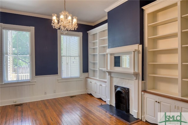 unfurnished living room featuring crown molding, hardwood / wood-style flooring, built in features, and an inviting chandelier