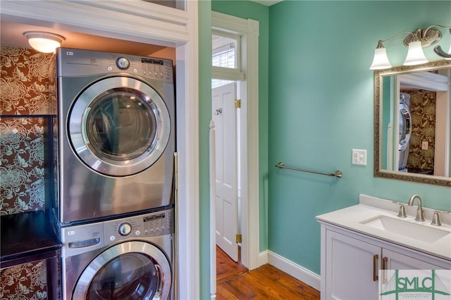 clothes washing area featuring wood-type flooring, stacked washing maching and dryer, and sink