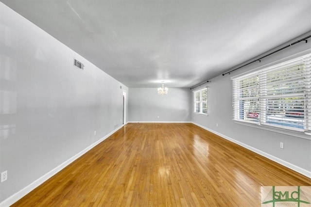 empty room with baseboards, light wood-style floors, visible vents, and a notable chandelier