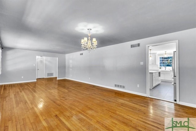 unfurnished living room with light wood-style floors, visible vents, and an inviting chandelier