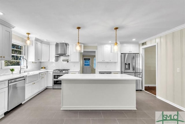 kitchen with pendant lighting, appliances with stainless steel finishes, white cabinetry, a kitchen island, and wall chimney exhaust hood