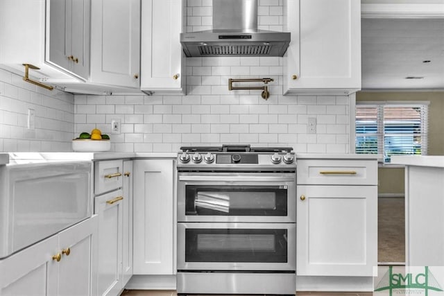 kitchen featuring double oven range, white cabinets, backsplash, and wall chimney exhaust hood