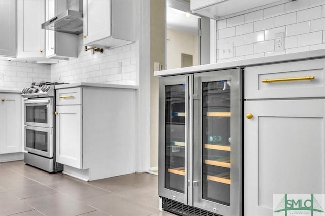 kitchen with tasteful backsplash, white cabinetry, wine cooler, range with two ovens, and wall chimney exhaust hood