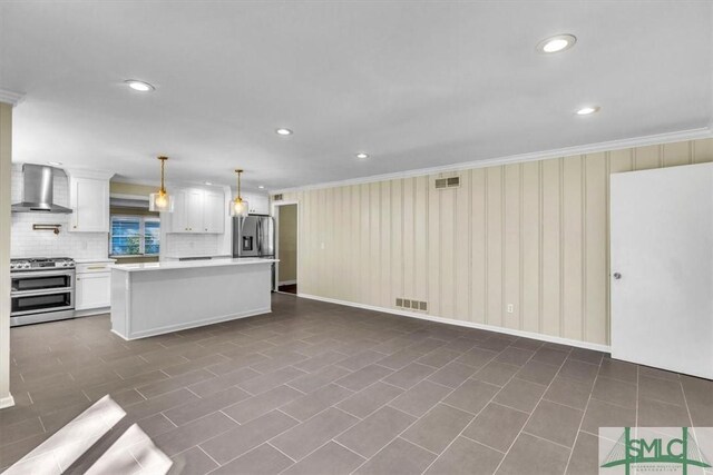 kitchen featuring stainless steel appliances, ornamental molding, white cabinets, decorative light fixtures, and wall chimney exhaust hood