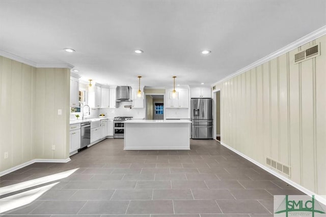 kitchen featuring wall chimney exhaust hood, white cabinetry, crown molding, hanging light fixtures, and stainless steel appliances