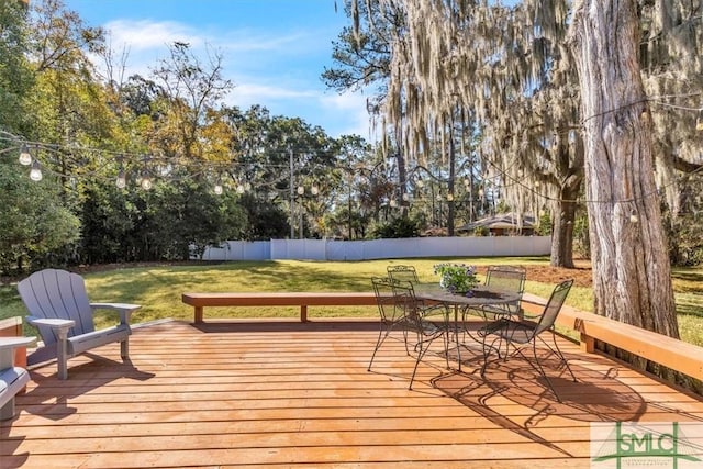 wooden deck with outdoor dining area, fence, and a lawn