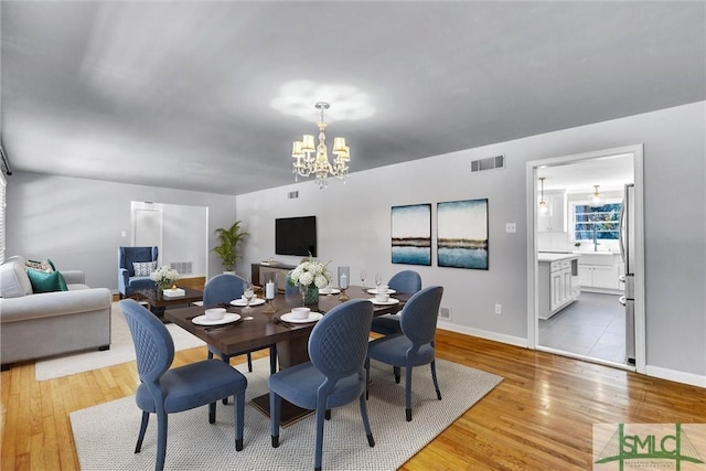 dining room with baseboards, light wood-style flooring, visible vents, and an inviting chandelier