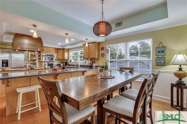 dining area featuring a raised ceiling, ornamental molding, sink, and light hardwood / wood-style flooring