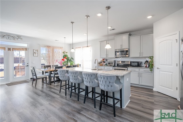 kitchen featuring decorative light fixtures, an island with sink, a breakfast bar area, backsplash, and stainless steel appliances