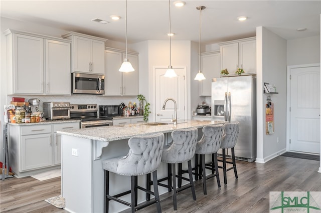 kitchen with appliances with stainless steel finishes, decorative light fixtures, sink, white cabinets, and a center island with sink