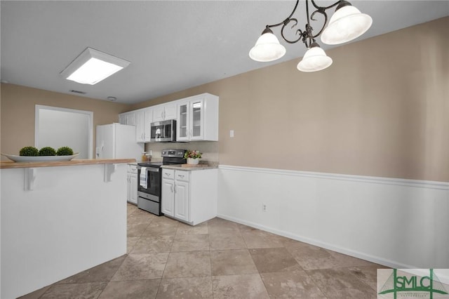 kitchen featuring white cabinetry, stainless steel appliances, a kitchen bar, decorative light fixtures, and kitchen peninsula