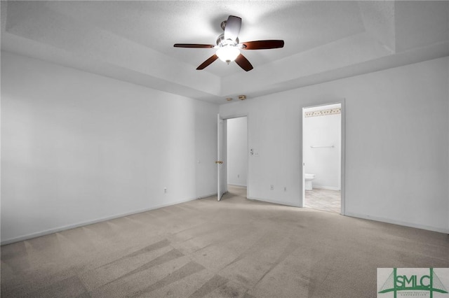 unfurnished bedroom with a raised ceiling, connected bathroom, light carpet, and ceiling fan