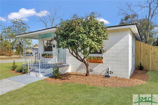 view of front of property with concrete block siding, a front yard, and fence