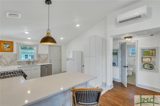 kitchen with a wall mounted air conditioner, a sink, stainless steel dishwasher, light wood-style floors, and light countertops