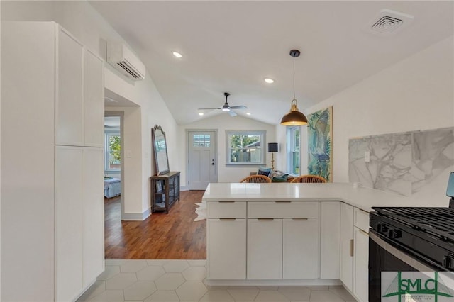 kitchen featuring visible vents, an AC wall unit, vaulted ceiling, range with gas stovetop, and a peninsula