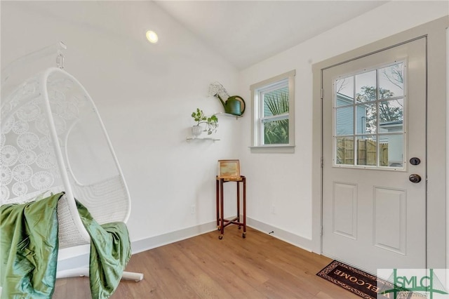 doorway featuring light wood finished floors, baseboards, and lofted ceiling