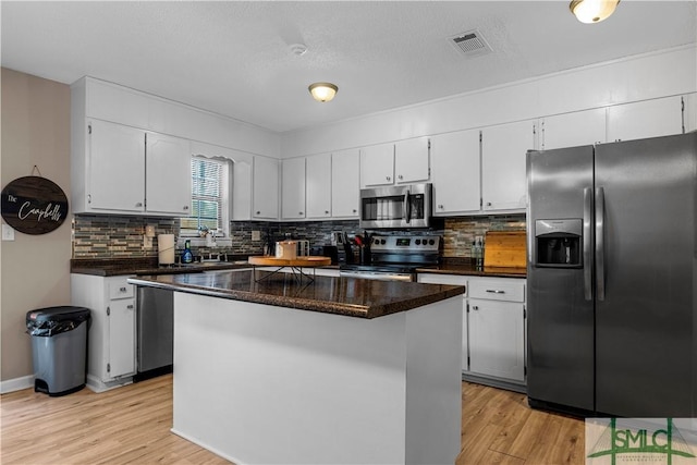 kitchen with white cabinets, decorative backsplash, a center island, stainless steel appliances, and light wood-type flooring