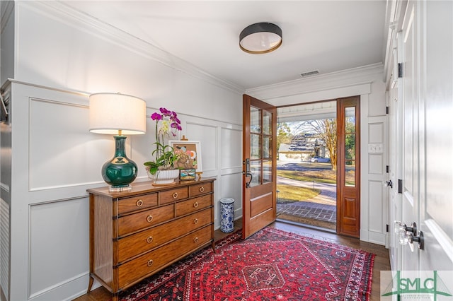 foyer entrance with a wainscoted wall, visible vents, ornamental molding, and a decorative wall