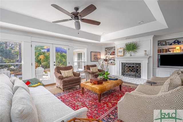 living room with built in shelves, a tray ceiling, and french doors