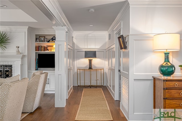 hallway featuring built in features, ornamental molding, wood finished floors, ornate columns, and a decorative wall