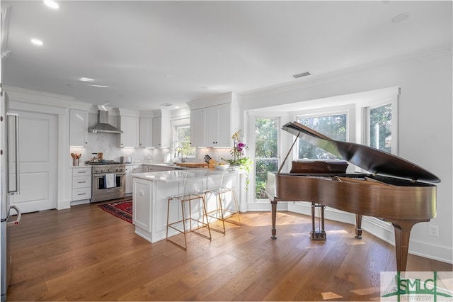 kitchen featuring high end stove, a peninsula, a breakfast bar, visible vents, and wall chimney range hood